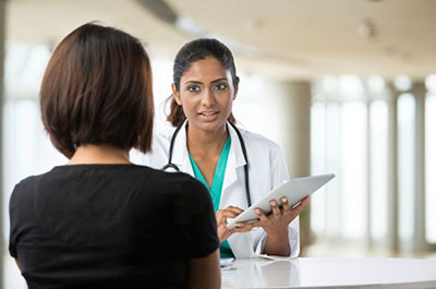 A woman doctor holding a clip board talking to a woman patient.