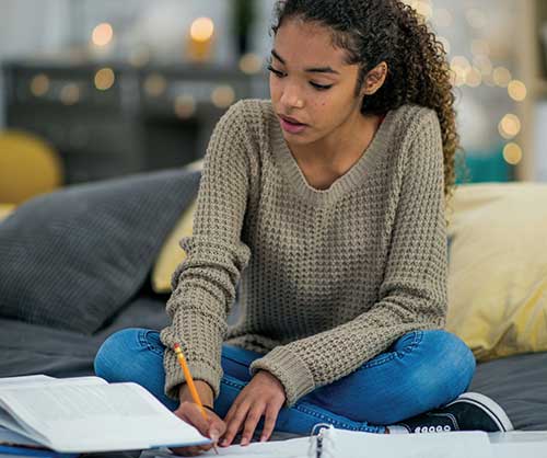 Teen girl sitting on her bed doing homework.