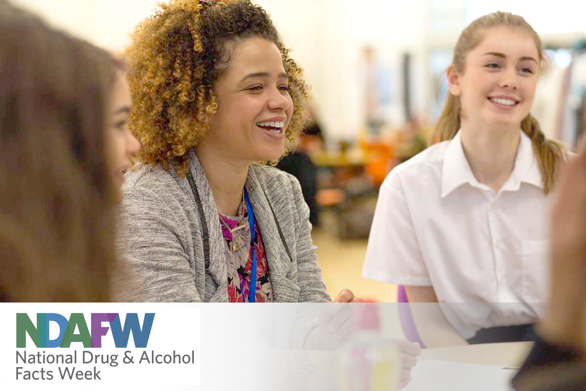 Young teacher sitting in a classroom and laughing with students; NDAFW logo