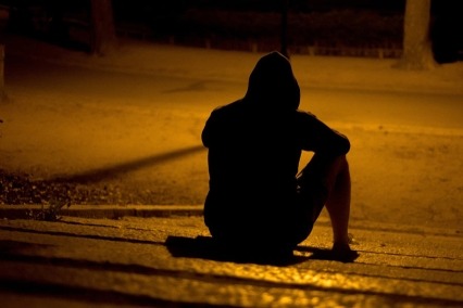Person in shadows sitting on curb