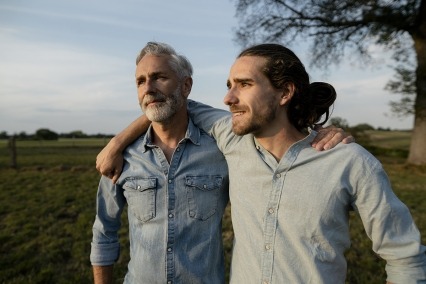 Father and adult son with arms around each other on a meadow in the countryside.