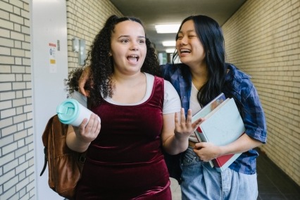 Dos adolescentes hablando y caminando juntas por el pasillo de un aula durante un día escolar.