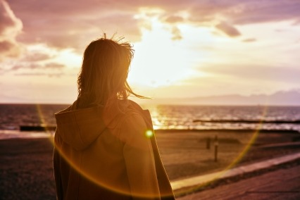 A young woman looking out on the beach at sunset.