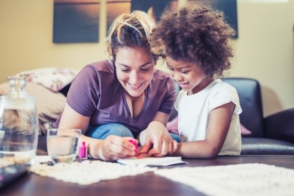 A young mother with her daughter sitting in the living room together and painting their nails.