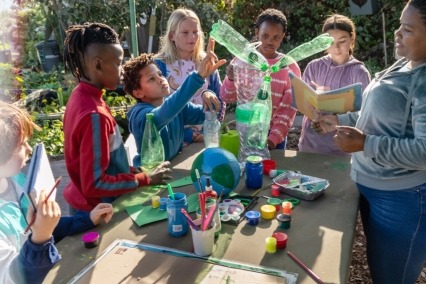 Un grupo diverso de seis niños haciendo arte ambiental al aire libre con un adulto.