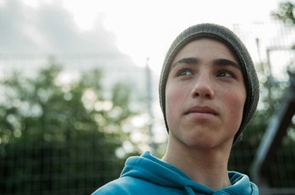 Adolescente afuera usando un gorro y mirando pensativamente lejos de la cámara.