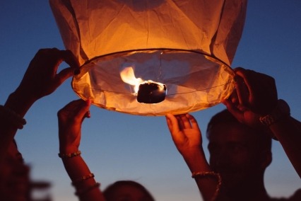 Group of people releasing a paper lantern into the sky at night.