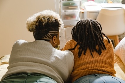 Vista trasera de madre e hija adolescente acostadas en la cama y leyendo juntas.