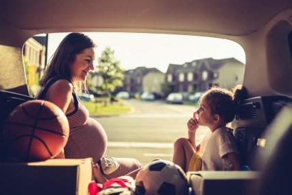 Expecting mother sitting in the back of a van with young daughter before a sports practice.