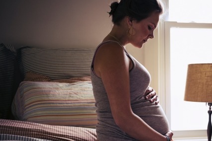 Una joven embarazada está sentada en la cama de su casa, sosteniendo tiernamente su vientre.