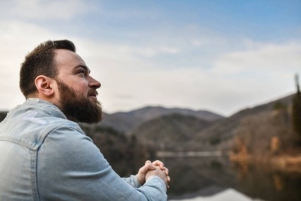 Man sitting outside and thoughtfully looking across a quiet lake during a clear sunny day.