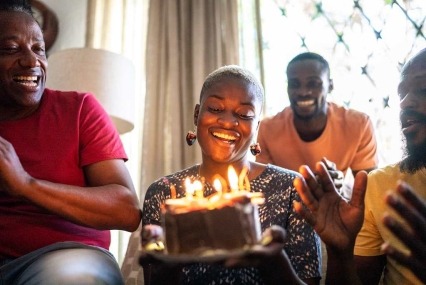 A young woman is holding a birthday cake and celebrating with family and friends.