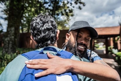 Two adult men standing outside and greeting and embracing each other.