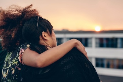 Rear view of two women sitting on a rooftop looking at the sunset.