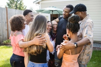 Multi-generational and diverse group of eight adults smiling and embracing.