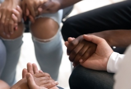 Diverse people sitting in circle holding hands at group therapy