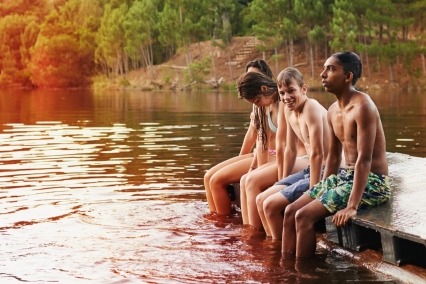 Group of teenage friends sitting on a pier out on a lake.