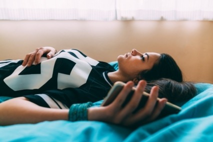 Girl lying on a bed with a cell phone in her hand. 