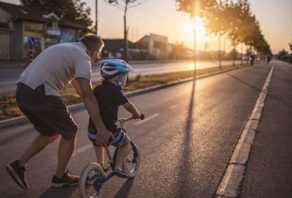 Adult man helping a young boy to ride a bike on a neighborhood street.