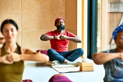Un hombre sentado con las piernas cruzadas y meditando en una clase de yoga. 