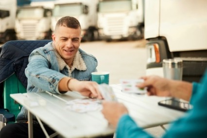 Man casually sitting outside during the day playing cards and drinking coffee.