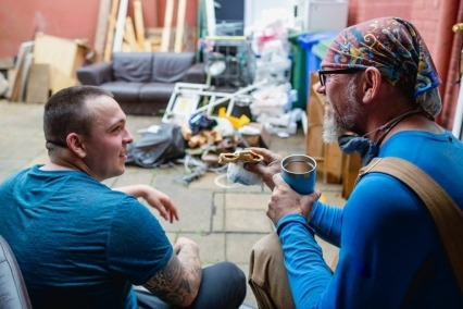 Rear view of two men wearing construction uniforms sitting down for a lunch break at a building renovation site.