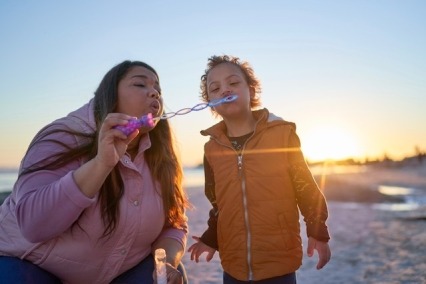 Mother and young son blowing bubbles on the beach at sunset. 