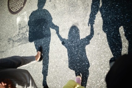 Shadow of two adults walking on a crosswalk and holding hands with a young child in between them.