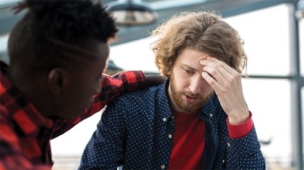 Worried man touching forehead while sharing his problems with colleague.