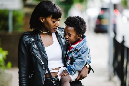 Black woman holding a toddler and walking down a city street.