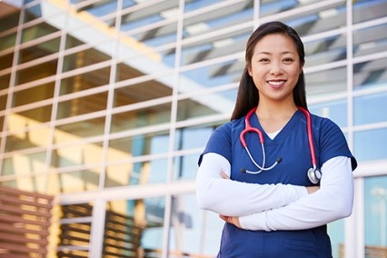 An Asian nurse standing in front of a building