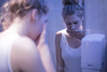 Image of a woman who is nauseated and standing in front of a mirror,