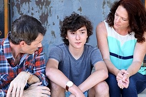Parents and their teen son talking with arms crossed.