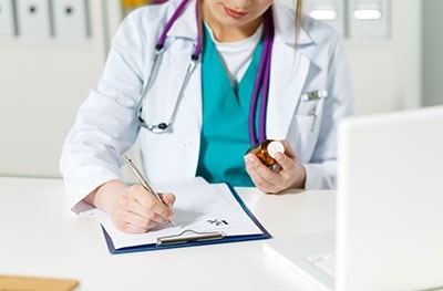 : Image of a female physician holding a bottle of medicine and taking notes. 