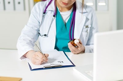 : Image of a female physician holding a bottle of medicine and taking notes.