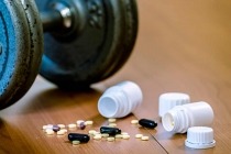 Steroid pills and capsules with dumbbell weight in the background
