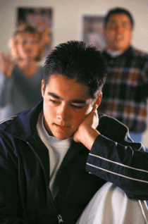 Foto de un joven estresado con sus padres parados detrás de él. 