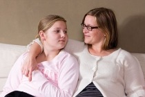 Mother draping arm over teenage daughter sitting on a couch