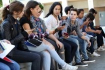 Diverse group of teens sitting on a bench looking at their cell phones.
