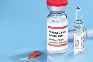 Fentanyl citrate injection ampule, vial, clear fentanyl dermal patch, and tablets on blue tray.