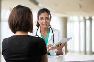 A woman doctor holding a clip board talking to a woman patient.