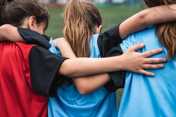 Rear view of three girls wearing sport uniforms standing and supporting each other.