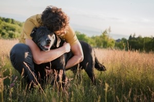Man in a grassy field hugging his dog.