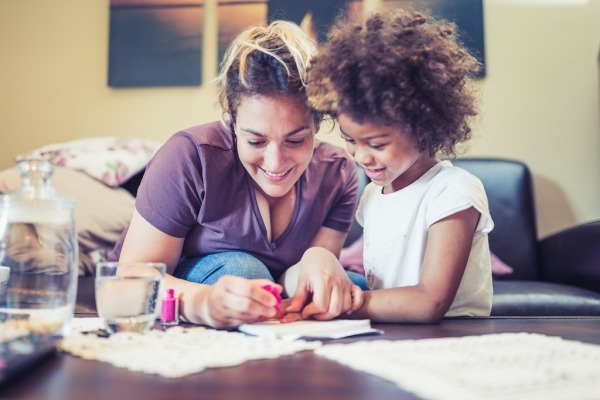 A young mother with her daughter sitting in the living room together and painting their nails.