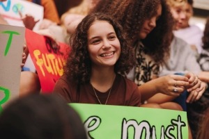 Close-up of teen girl holding a poster at crowded youth rally.