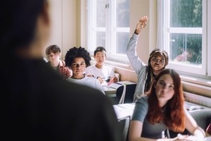 Teen girl raising her hand to ask the teacher a question during class.