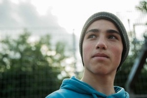 Teenage boy outside wearing a beanie cap and looking thoughtfully away from the camera.