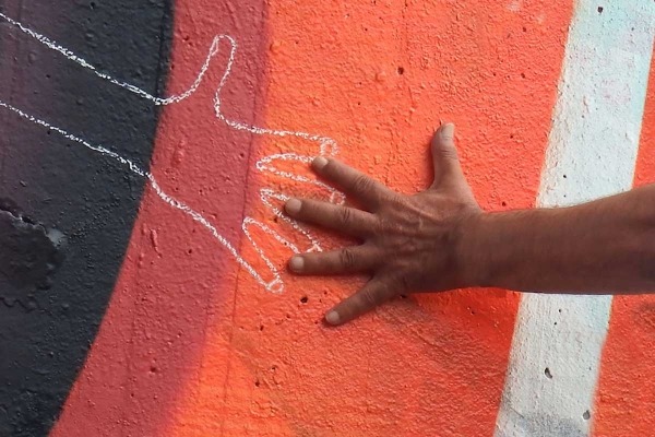 Close-up of a hand placed palm down on concrete reaching across to touch a chalk drawing of a hand.