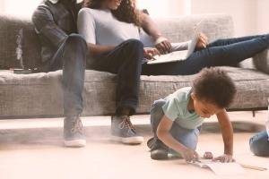 A photo of an African American parents sitting on a sofa while their child plays on the floor