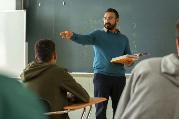 A male teacher standing in front of a chalkboard talking to his students